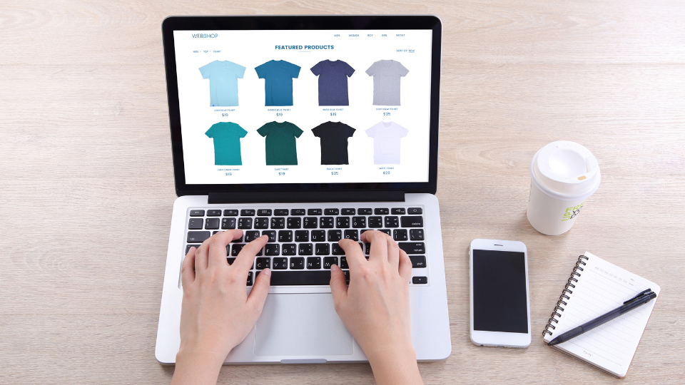 Hands typing on a laptop setting up dynamic pricing for t-shirts displayed on the screen