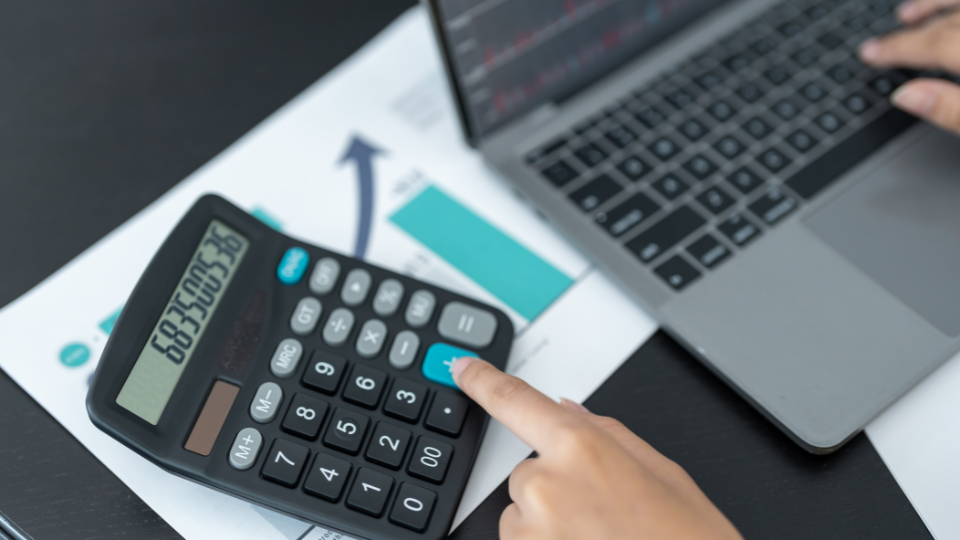 A person using a calculator and laptop on a desk, calculating Walmart Fulfilment Services costs